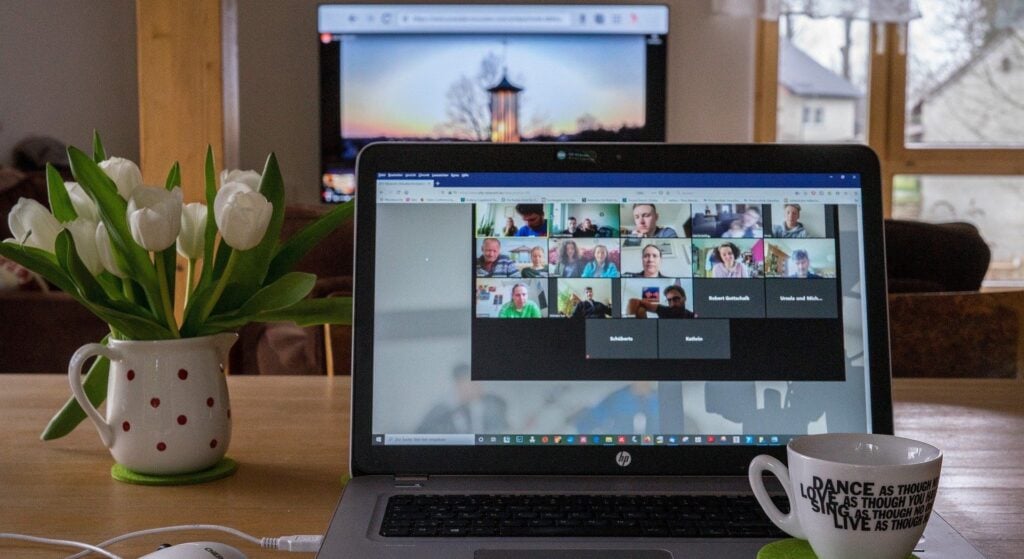 Un ordinateur portable affichant une salle de réunion virtuelle placé sur une table, un pot de fleurs, un café et une souris d'ordinateur à ses côtés.